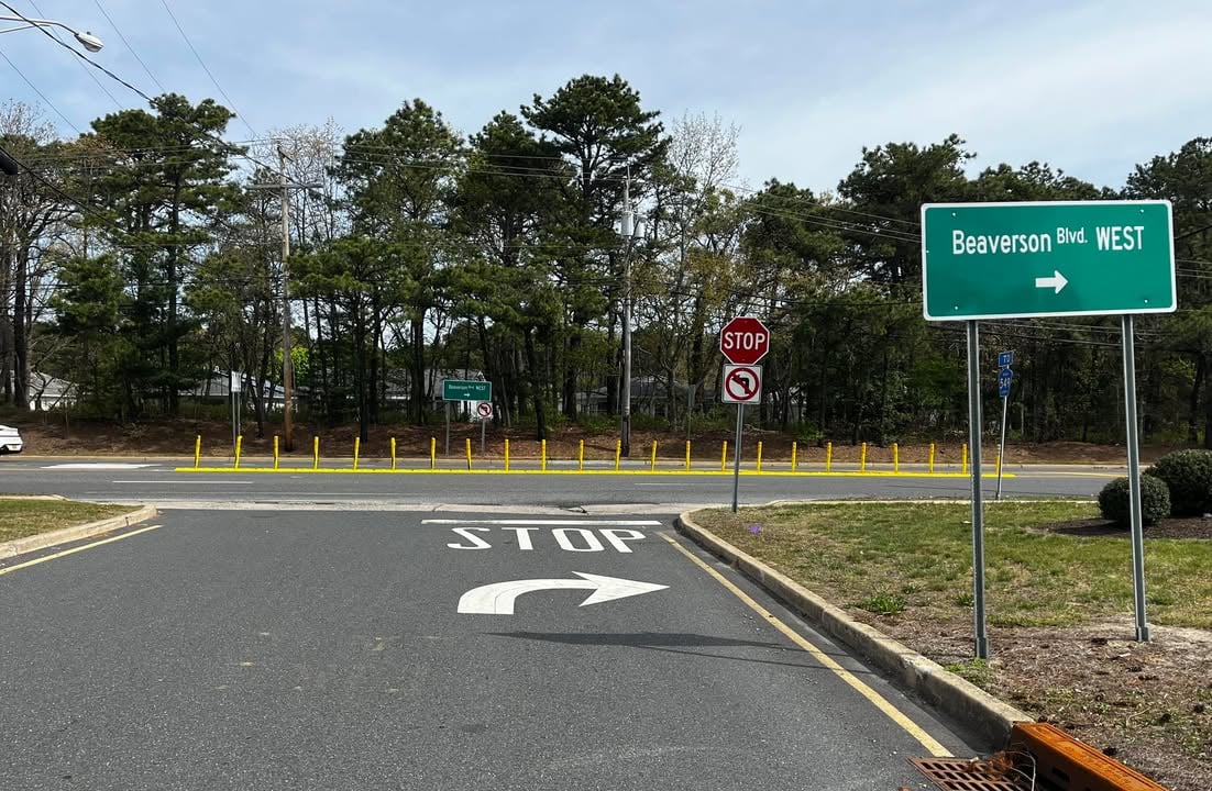 Intersection scene: STOP painted on the road with a curved right-turn arrow, crossing into a divided street with yellow bollards and a Beaverson Blvd West sign on the right.
